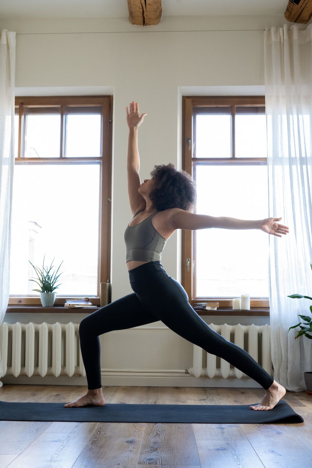 A woman stretching on a yoga mat beside a bright window at home