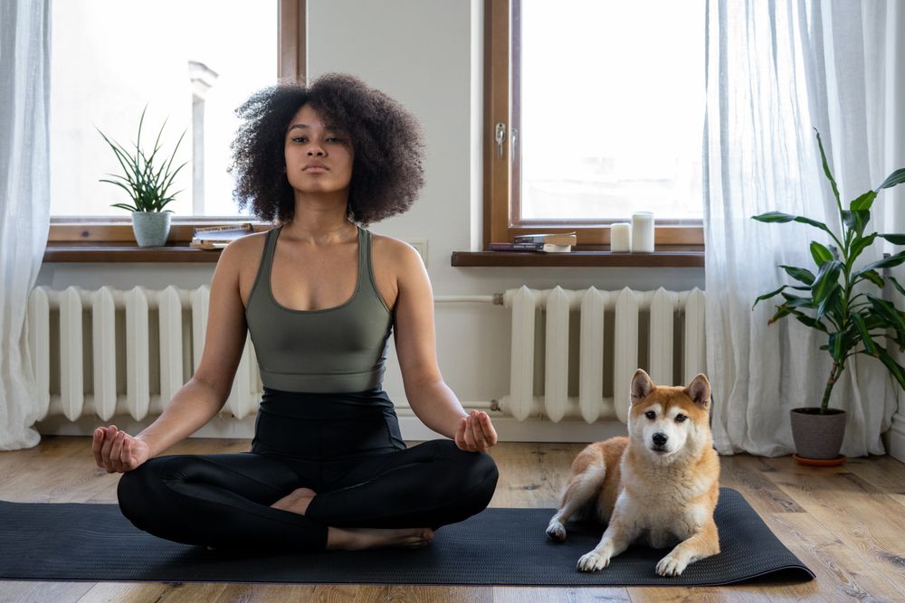 A woman sitting comfortably on a mat at home with her dog
